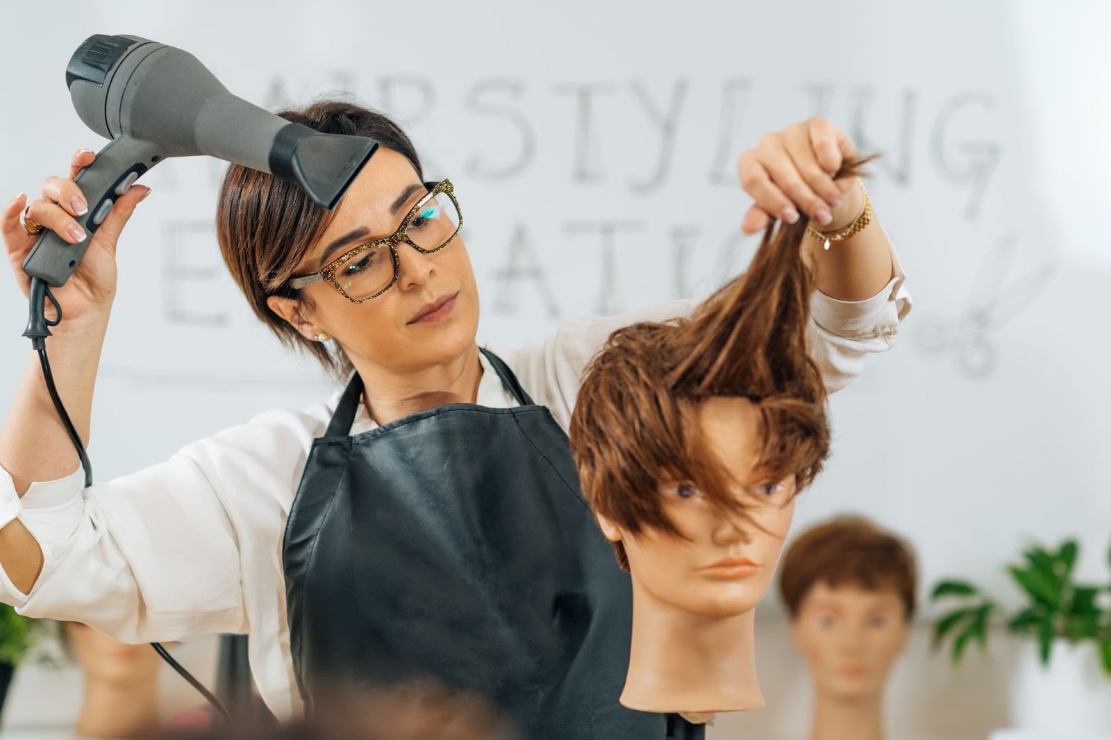 Hairstyling for Men vs. Women: What’s the Difference? 1 Female instructor blow-drying mannequin hair during cosmetology training