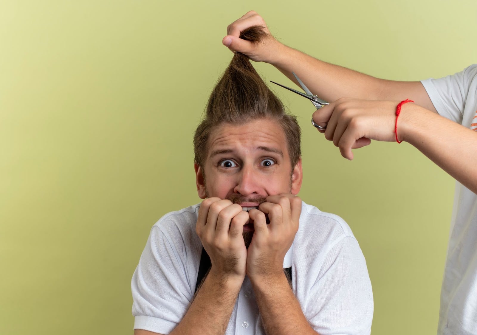 Nervous man biting his nails as someone prepares to cut his hair with scissors, humorous barbershop moment