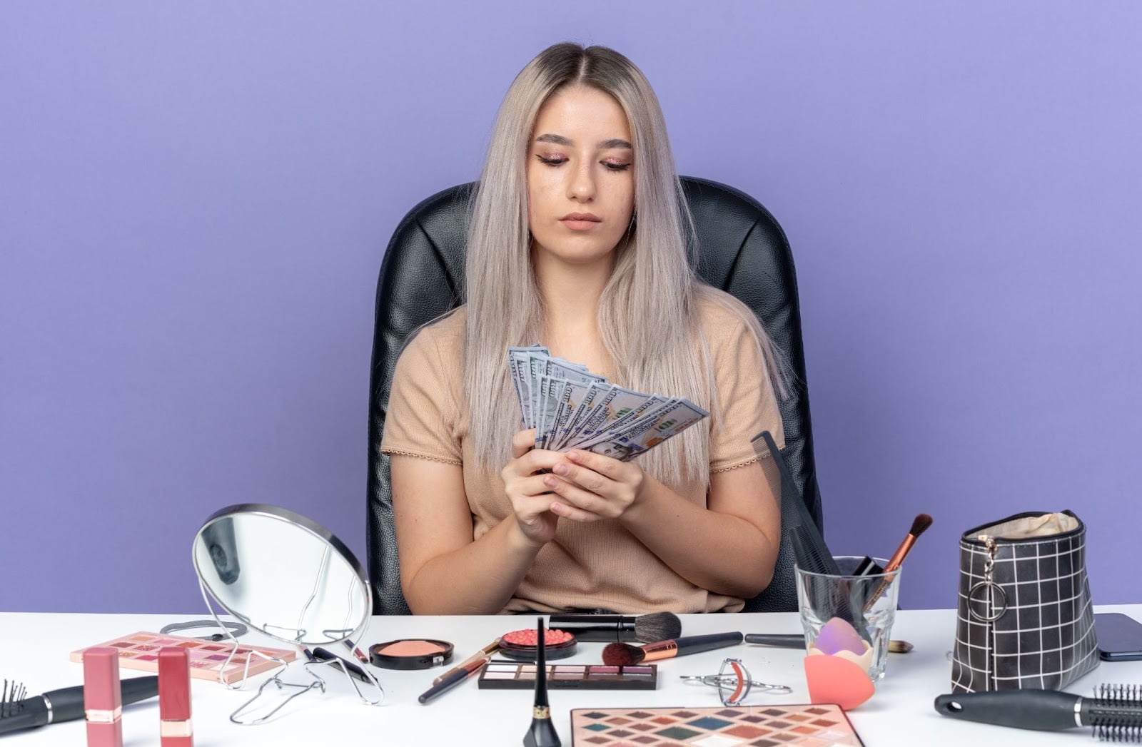 How to Choose a Beauty School: A Complete Guide 4 Young cosmetology student counting dollar bills at her makeup station, surrounded by beauty products.