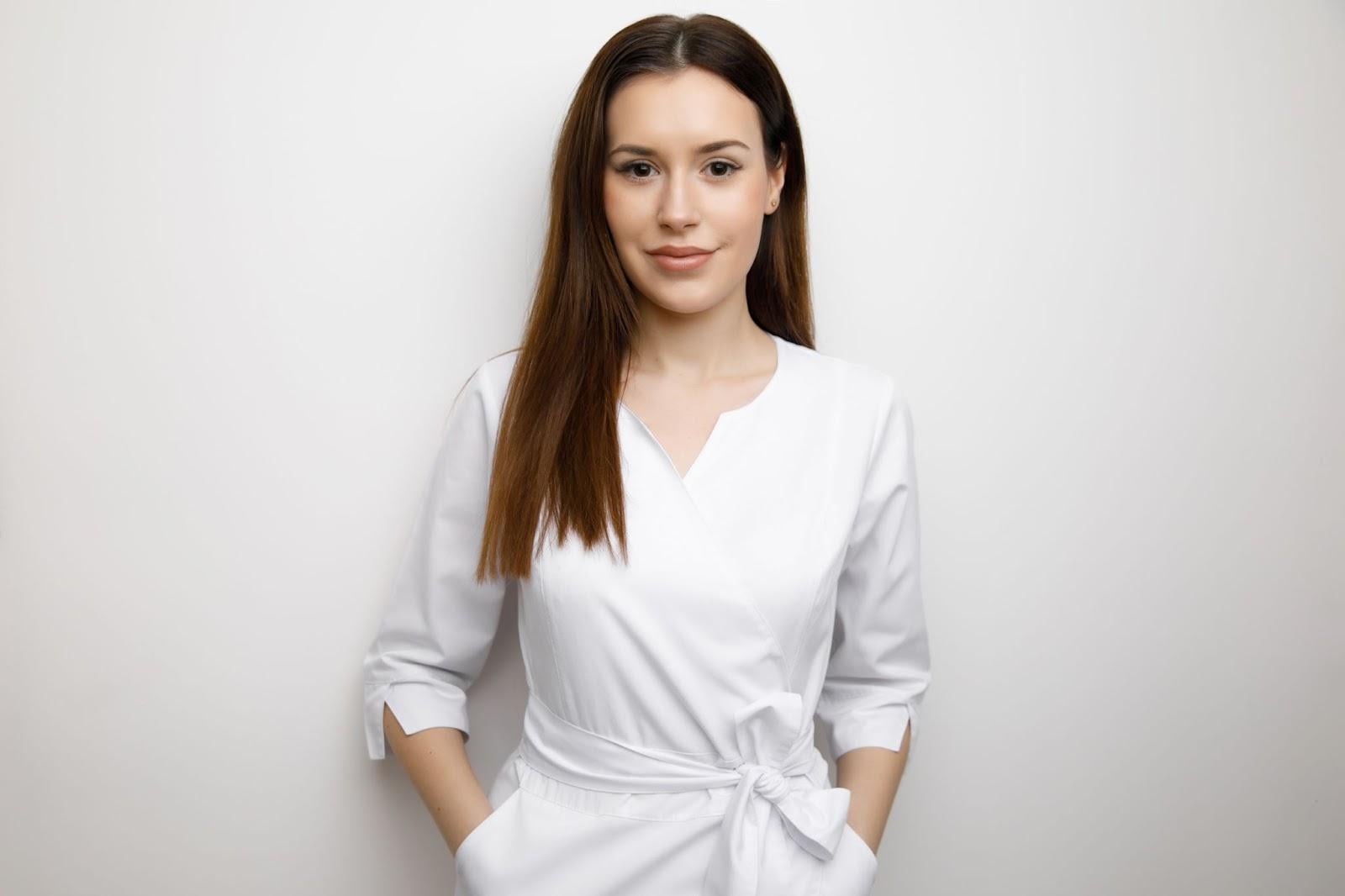 Portrait of a confident cosmetologist wearing white uniform standing against white background