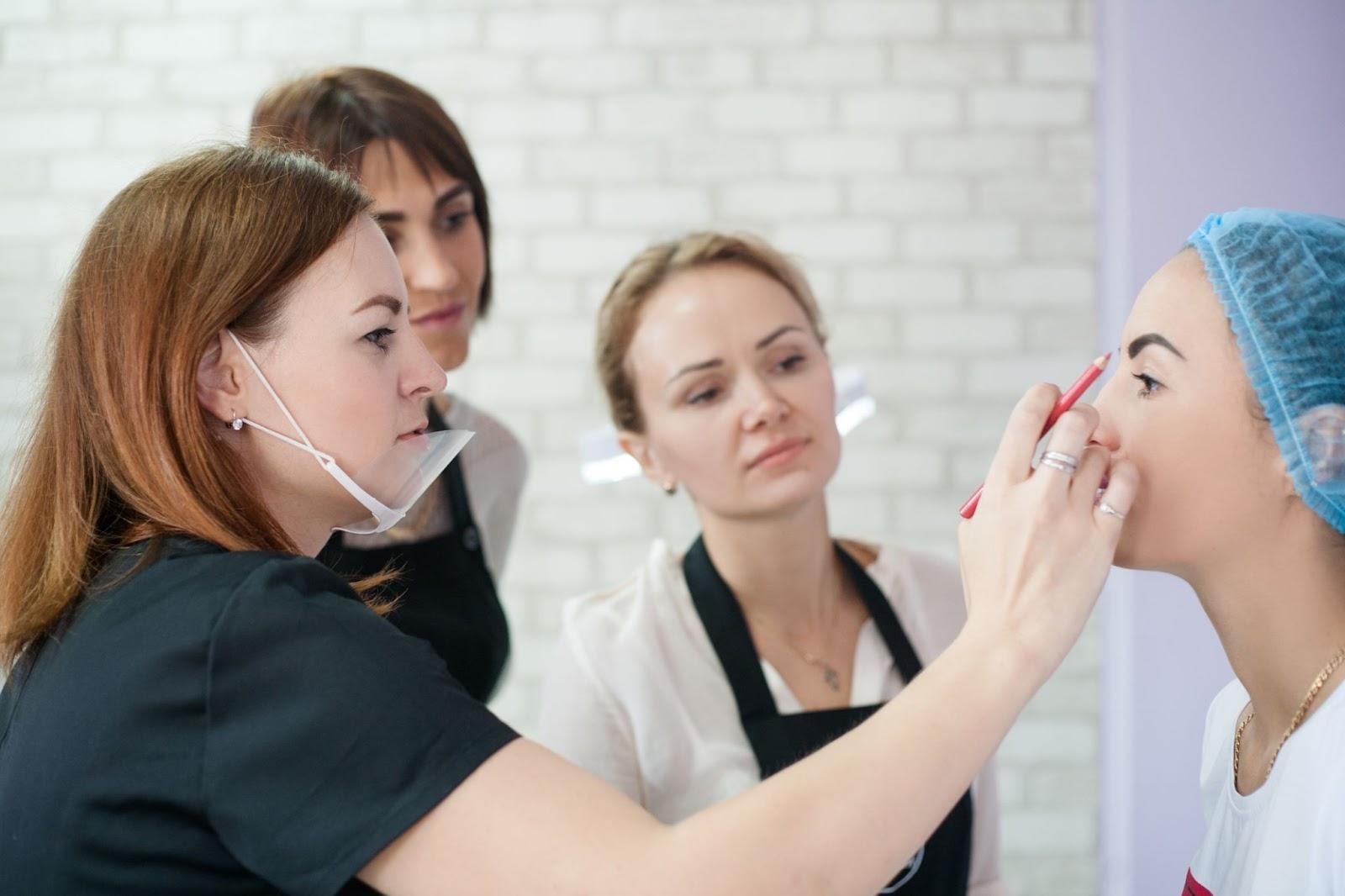 Beauty students observing instructor applying makeup on model during training session