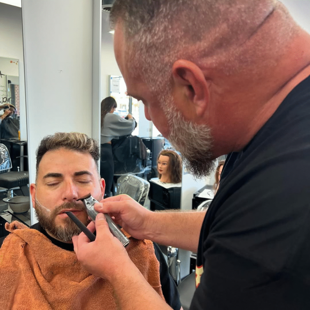 Professional barber shaping client’s beard with clippers in barbershop