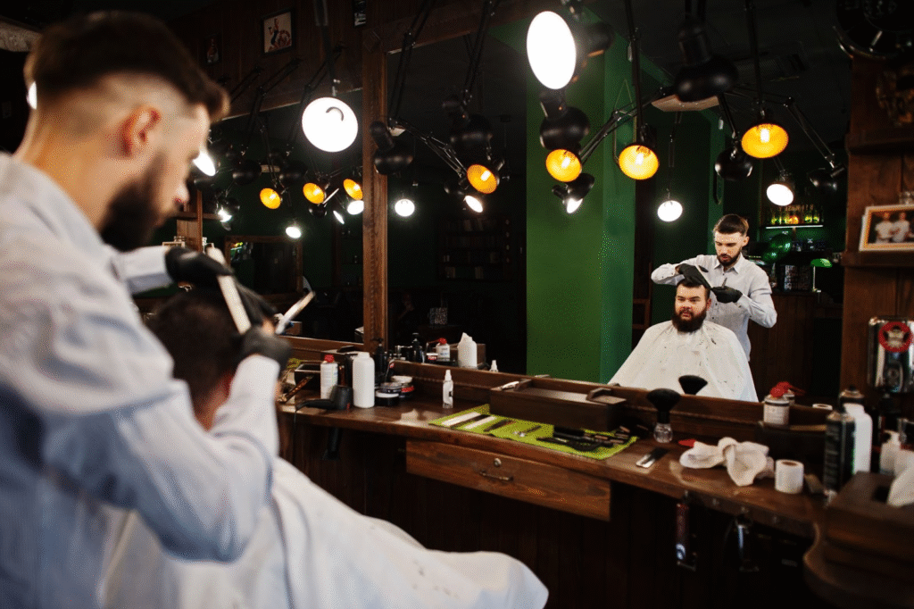 Cosmetologist vs. Esthetician vs. Barber: Choosing the Right Beauty Career Path 4 Barber cutting client’s hair in traditional barbershop with mirrors and lights